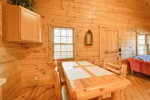 A wooden cabin interior with a dining table, chairs, a cabinet, and a bed.