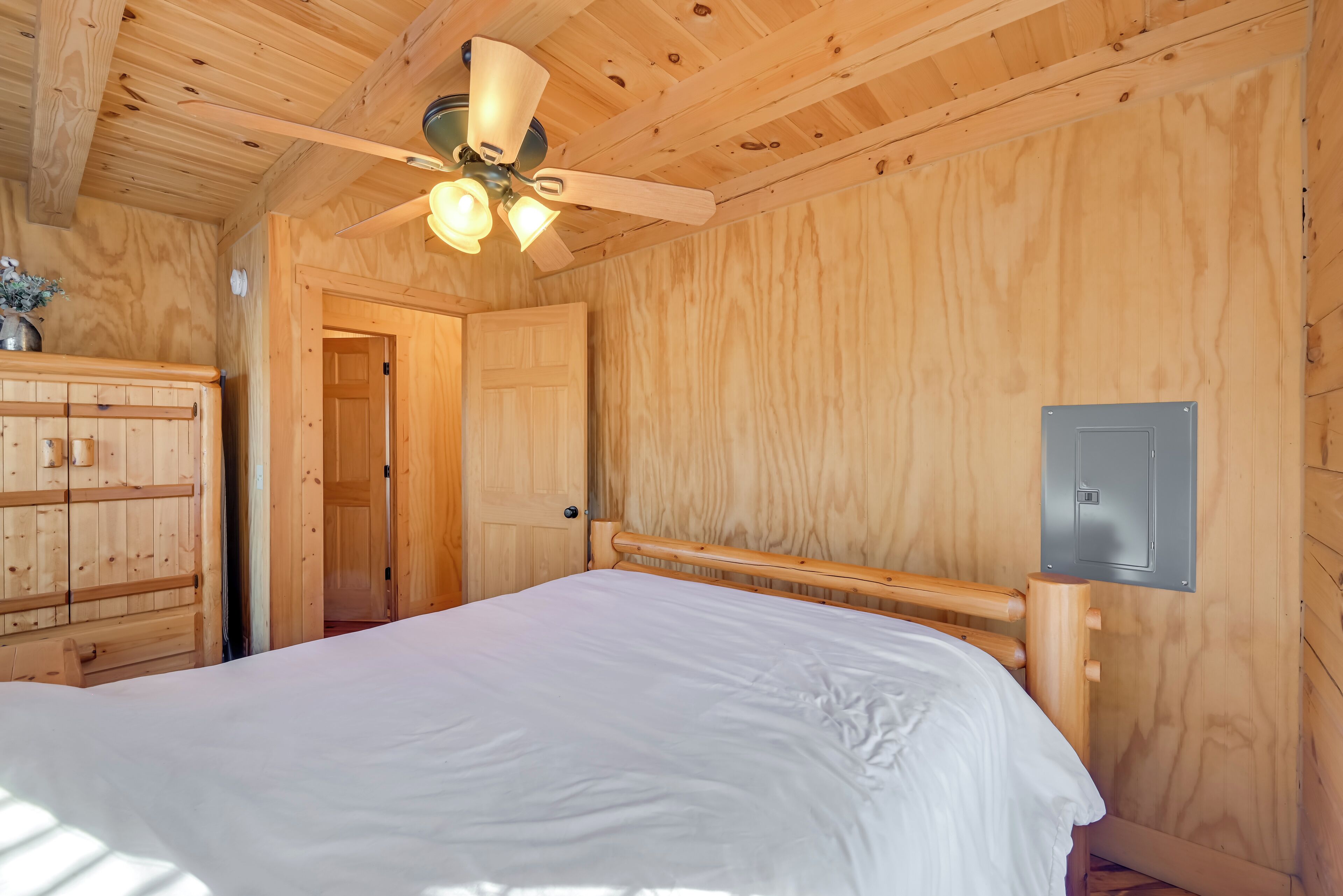 A wooden room with a bed, a ceiling fan, and a door.