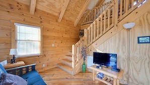 L’intérieur d’un chalet en bois, avec un escalier, un canapé, un téléviseur et une lampe.