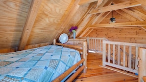 Un intérieur en bois avec un lit, un ventilateur et une petite table agrémentée de fleurs.