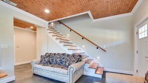 Un salon moderne avec un canapé de couleur claire, un plaid à motifs et un escalier en bois doté d’un système d’éclairage intégré.