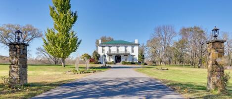 A large, stately building with a green roof, a central entrance, and a paved driveway leading to it.