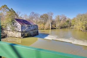 A rustic wooden building by a calm river, surrounded by trees and a clear sky.