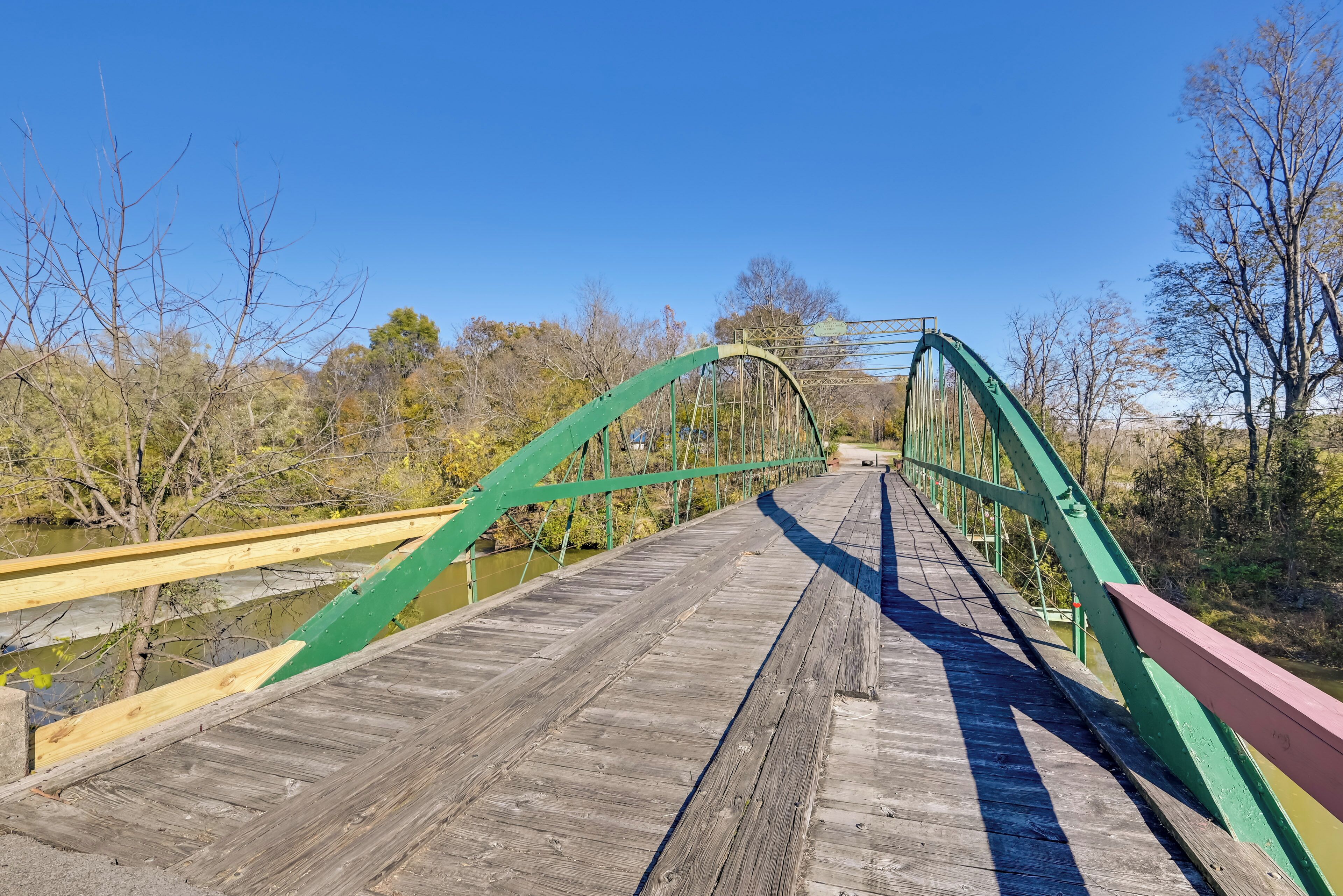 A wooden bridge with green railings and a river below.