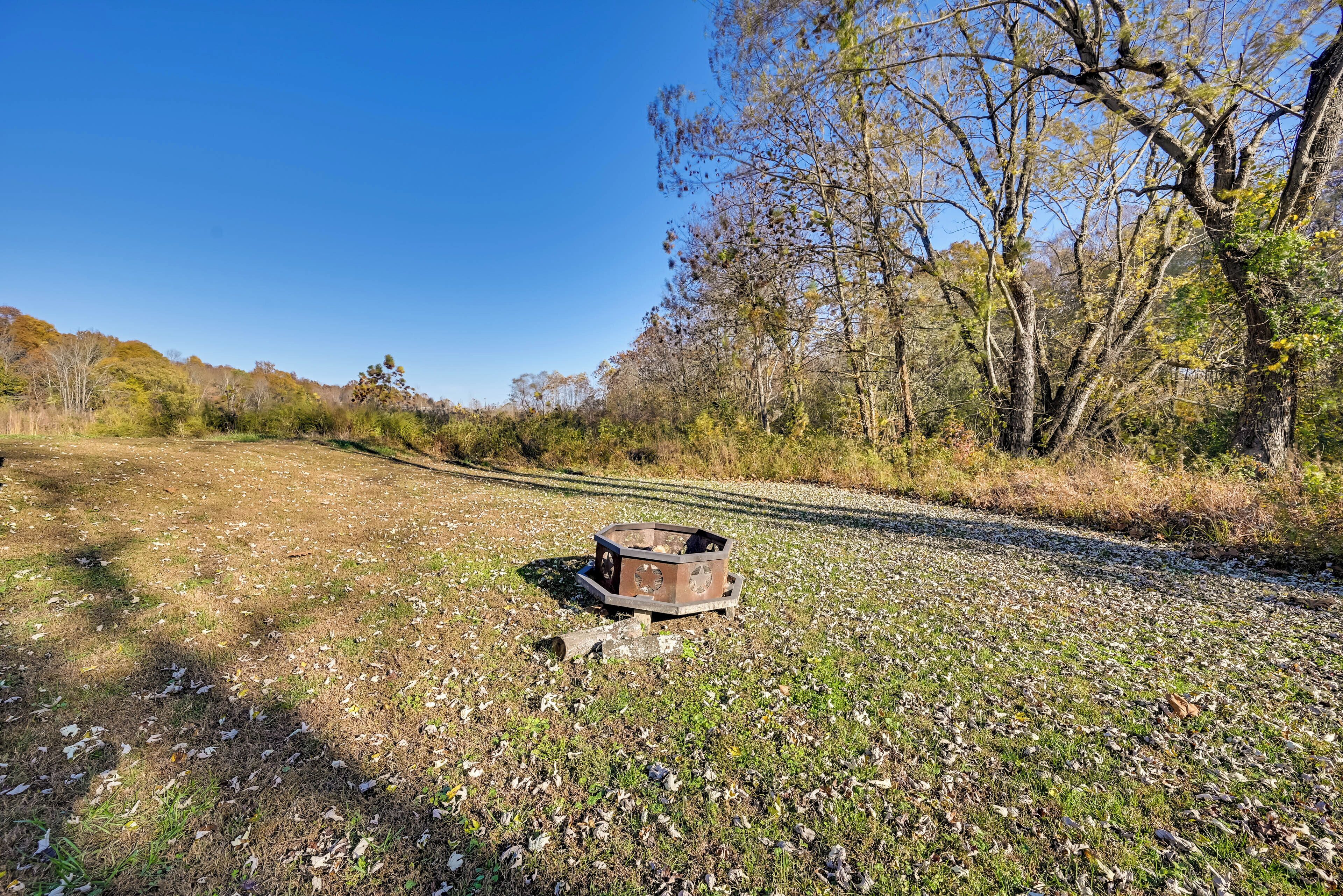 An outdoor area with a metal structure, possibly a trash bin, surrounded by trees and a gravel path.