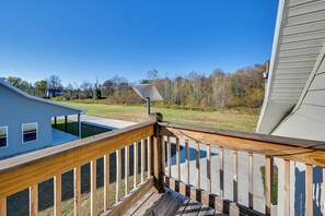 A wooden deck with a solar panel, a pool, and a grassy yard with trees.