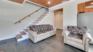 A modern living room with a staircase, two patterned sofas, and a kitchen area. - Fish & Unwind! Rough River Hideaway w/ Deck (Falls of Rough)