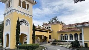 A yellow building with a tower, arched windows, and a covered walkway.
