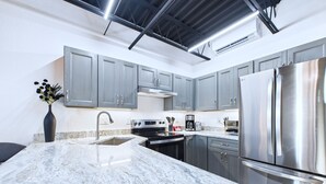 A modern kitchen with grey cabinets, a stainless steel refrigerator, and a marble countertop. - Experience modern elegance at Mangrove Lofts—steps from Port Canaveral and minutes to Cocoa Beach. Enjoy sleek design, premium comfort, onsite cruise parking avail, easy access to beaches, and rocket launch views from inside unit! (Cape Canaveral)
