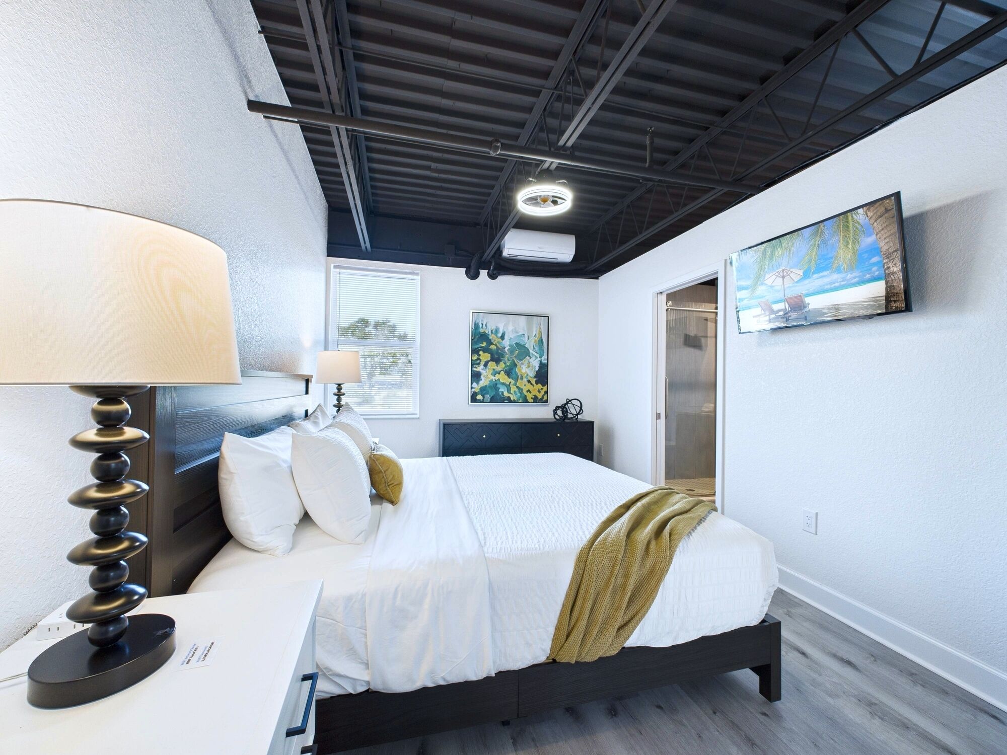 A modern bedroom with a bed, bedside lamps, a painting, and a window.