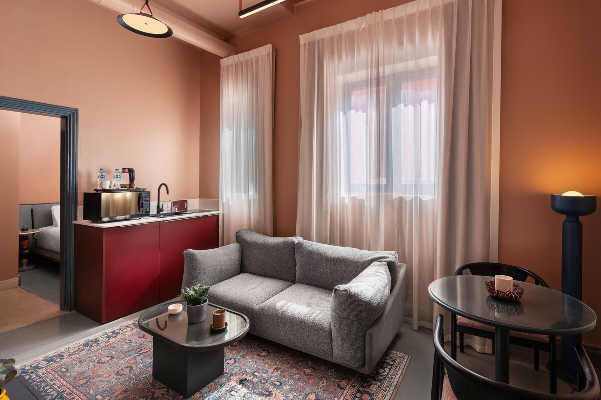 Una sala de estar moderna con un sofá gris, una mesita de centro pequeña, un mueble de almacenamiento rojo y una mesa de comedor con sillas.