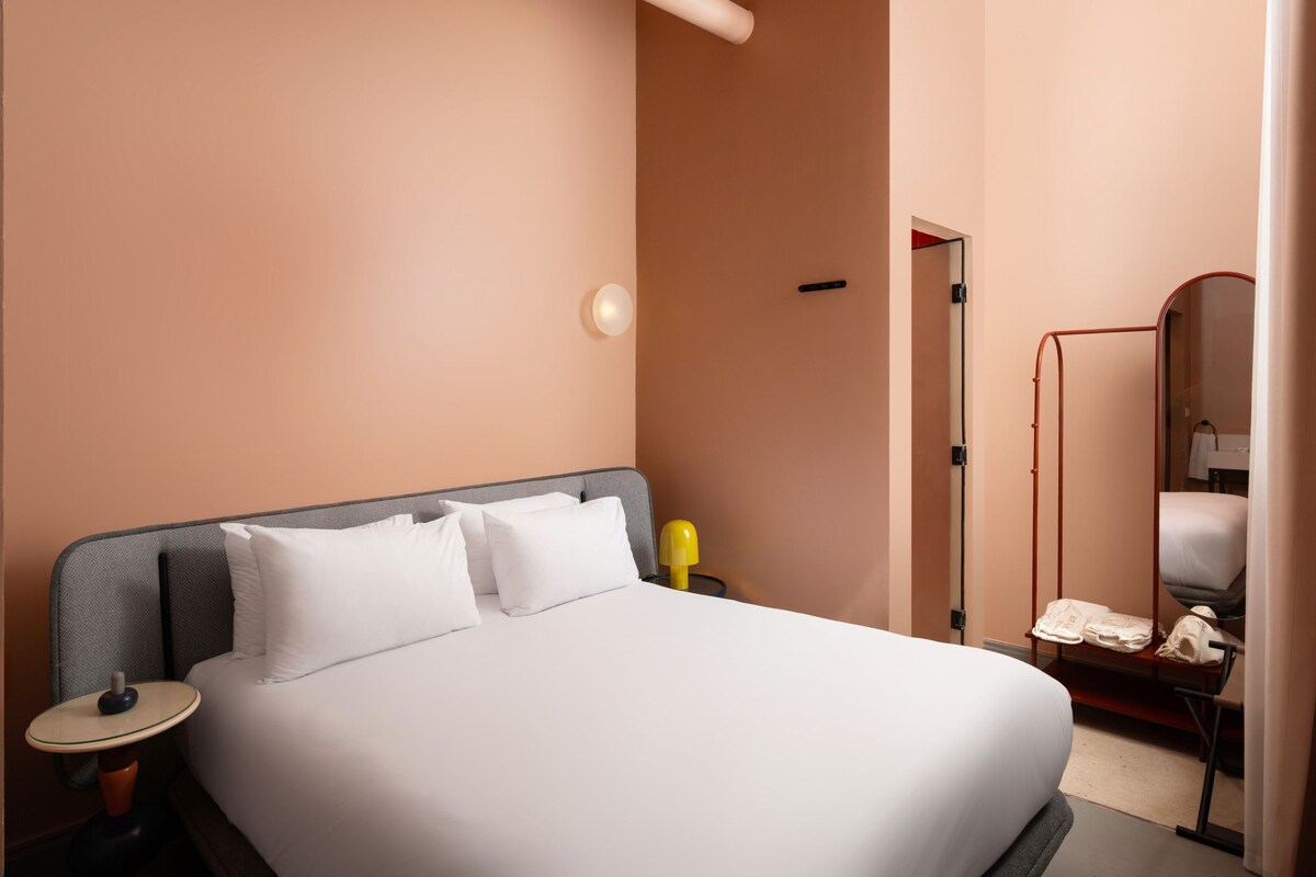 Una habitación de hotel con una cama grande, una mesita de noche, una lámpara y un espejo.