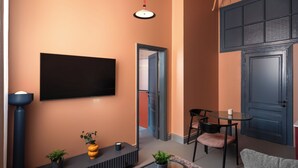 A modern living room with a flat-screen TV, a small table with chairs, a potted plant, and a decorative vase. - Brassbell grey apartments Bidair House (Cairo)
