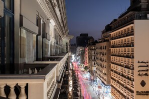 Un paisaje urbano nocturno con un edificio que muestra un letrero destacado que dice "ELNASSI" y una vista de una calle concurrida con estelas de luz dejadas por vehículos en movimiento.