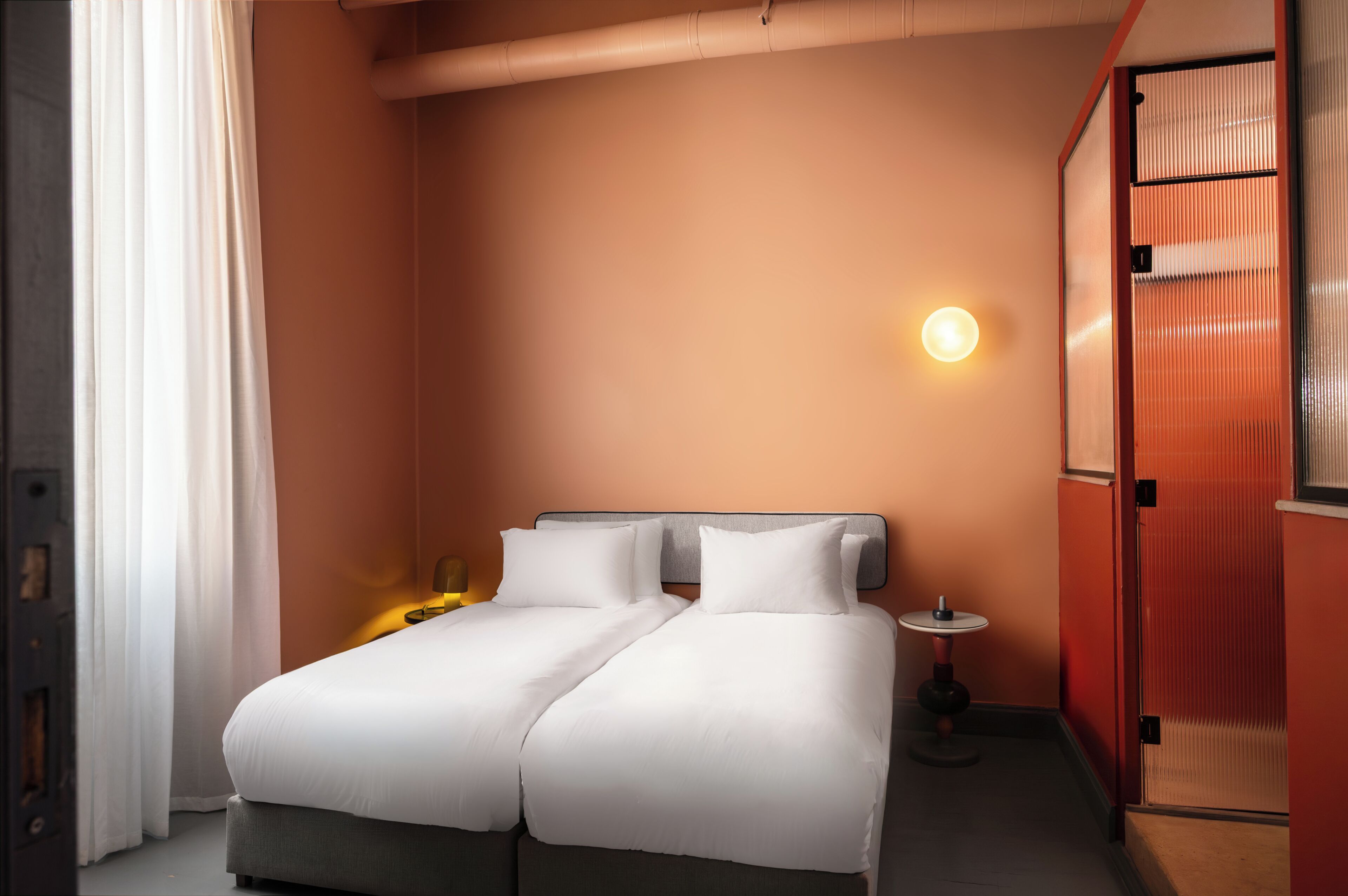 A double bed with white bedding, a bedside table with a lamp, and a wall-mounted light fixture.
