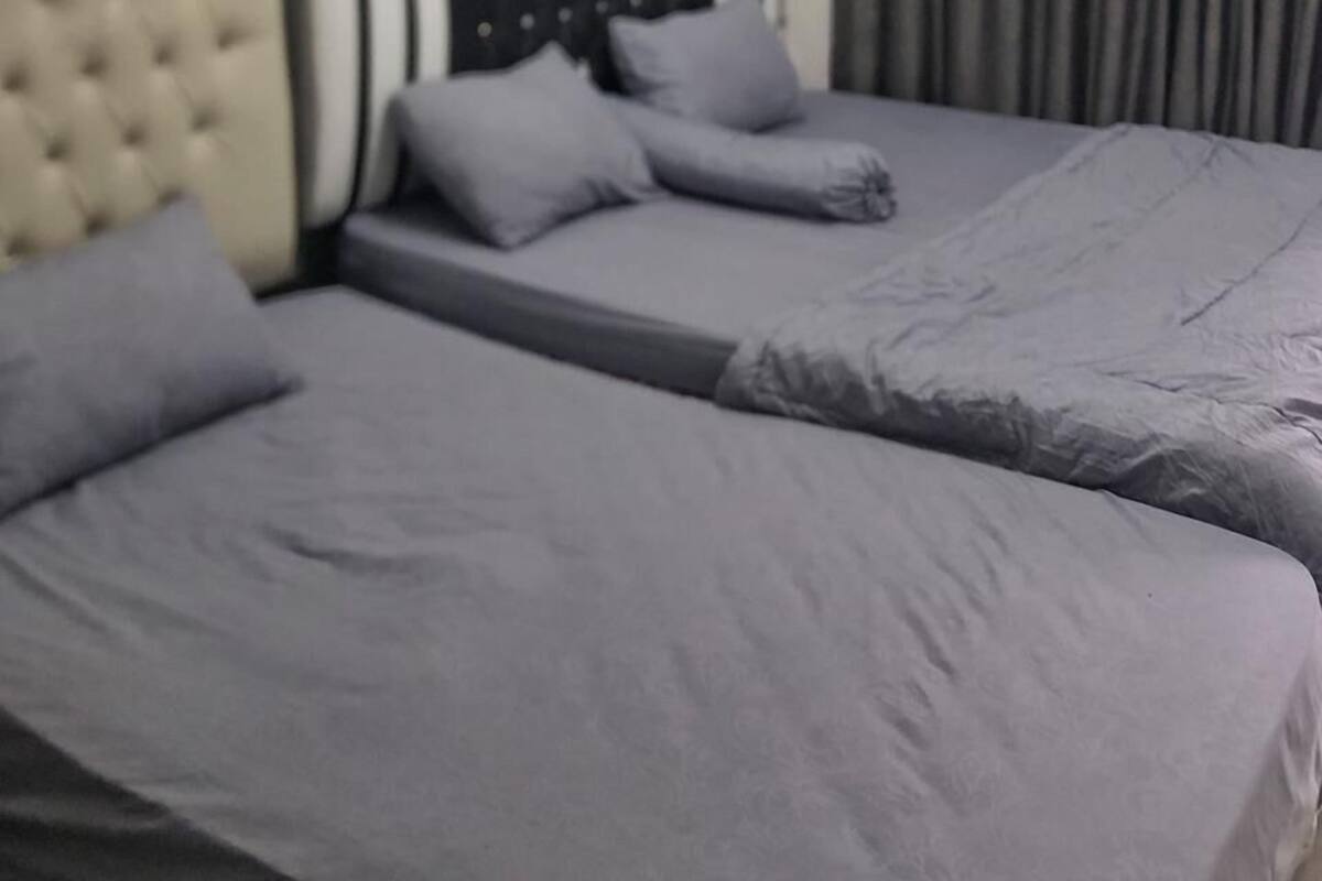 A bedroom with two beds, a tufted headboard, and a window with curtains.