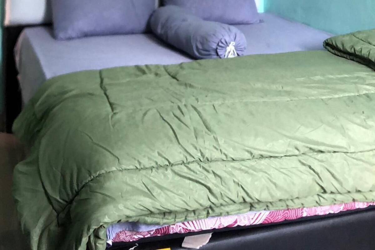 A bed with a green blanket and two pillows, a tufted headboard, and a plain wall.
