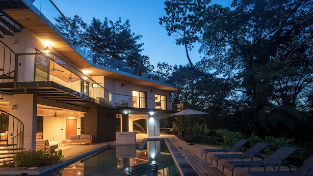 Une maison moderne dotée d’une piscine, d’un espace salon extérieur et d’un escalier menant à un étage supérieur.