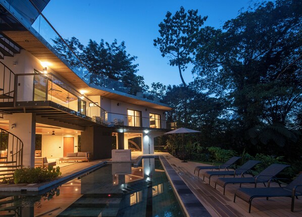 Une maison moderne dotée d’une piscine, d’un espace salon extérieur et d’un escalier menant à un étage supérieur.