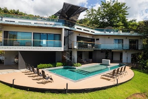 A modern house with a swimming pool, outdoor seating, and a staircase leading to a balcony.