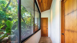 Un couloir avec une porte en bois, un mur de verre donnant sur un paysage verdoyant et un sol à motifs.