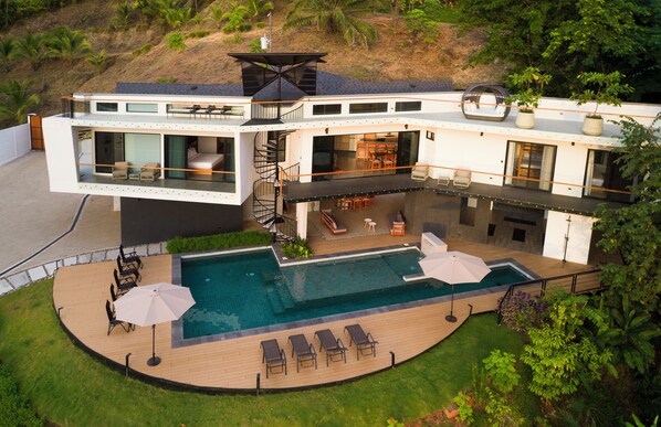 A modern two-story house with a large outdoor swimming pool, a covered patio, and a spiral staircase.