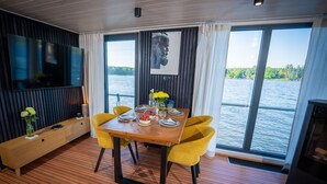 Un comedor con una mesa de madera, sillas amarillas, un televisor de pantalla plana y un ventanal con vistas al agua.
