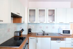 Une cuisine avec des meubles blancs, un grille-pain, une bouilloire, un four à micro-ondes et un lave-vaisselle.
