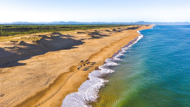 Ein Strand mit freiem Blick auf den Ozean, einem Sandweg und Fußspuren, die zum Wasser führen.