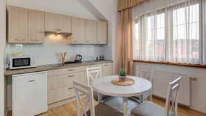 A compact kitchen with a microwave, kettle, and white cabinets. There is a dining table with chairs and a potted plant. - Willa Drako (Międzyzdroje)