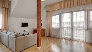 A spacious living room with a wooden ceiling beam, a sofa, a small table with a plant, and large windows with sheer curtains. - Willa Drako (Międzyzdroje)