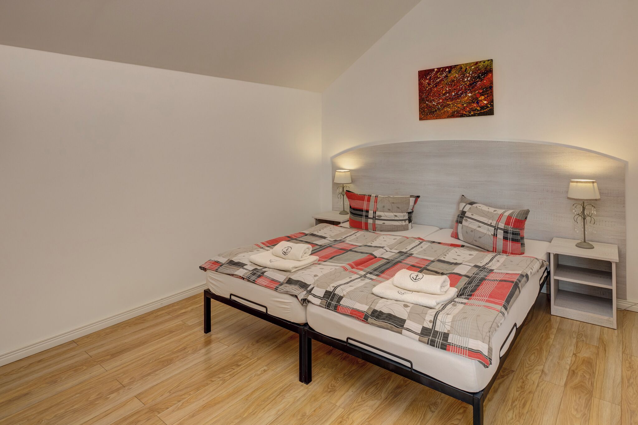 A bedroom with a bed, two bedside tables, a nightstand, and a painting on the wall.