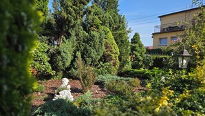 A garden with various plants and a statue. There is a building in the background. - Willa Drako (Międzyzdroje)