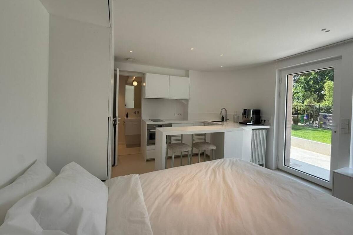 A modern bedroom with a large bed, a kitchenette, and a sliding door to a balcony.