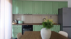 Uma cozinha com armários verdes, uma geladeira de aço inoxidável, uma mesa de madeira e um vaso com flores.