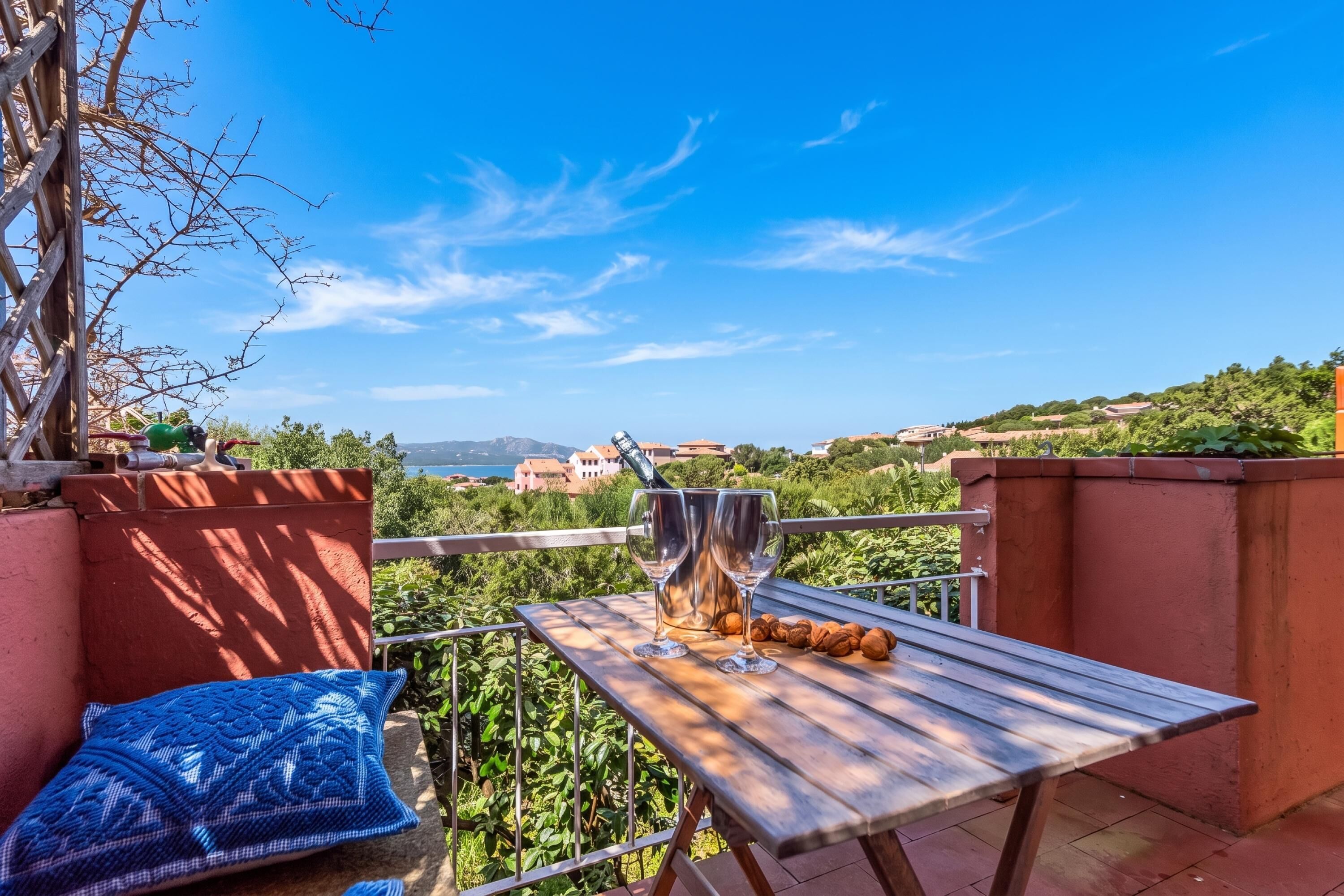 A wooden table with two wine glasses and walnuts, set against a scenic backdrop of hills and a clear sky.