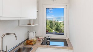 A kitchen with a window view of a mountainous landscape, a sink, a coffee maker, and a plate of croissants. - Aironi 34 (Olbia)