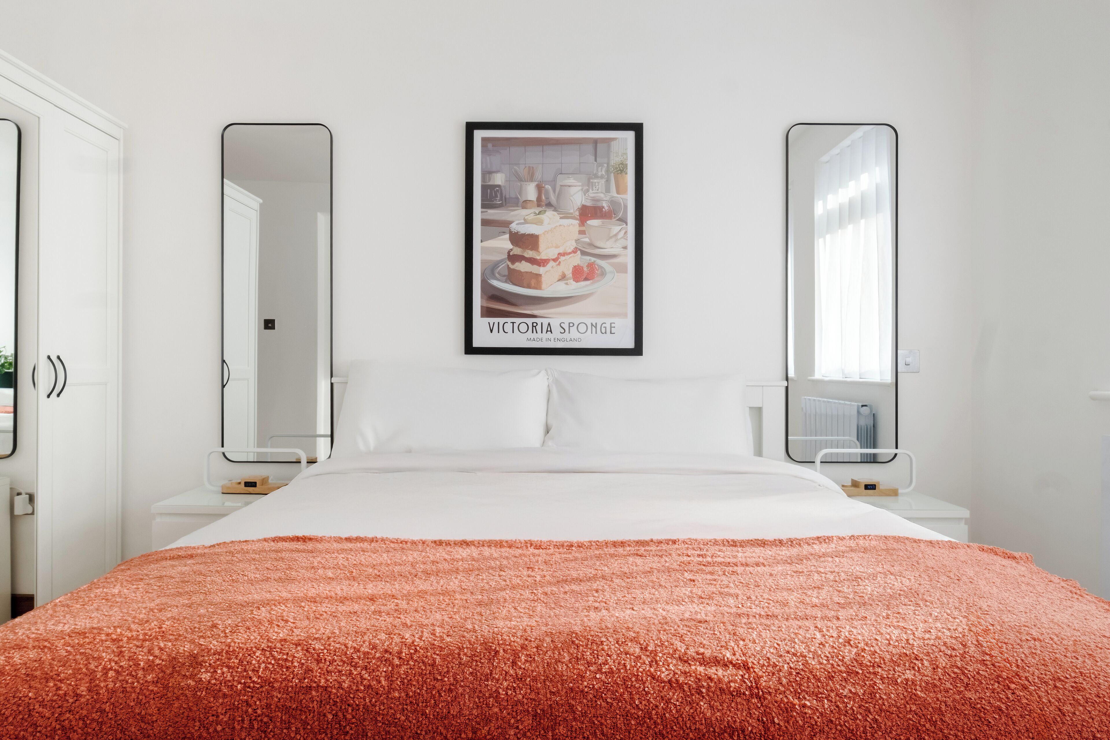 A hotel room with a bed, two bedside tables, a framed picture on the wall, and two mirrors on the bedside tables.
