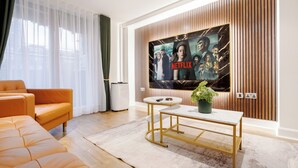 Ett modernt vardagsrum med en stor platt-TV som är monterad på en väggpanel av trä, en bekväm orange soffa, ett litet runt soffbord och en krukväxt.