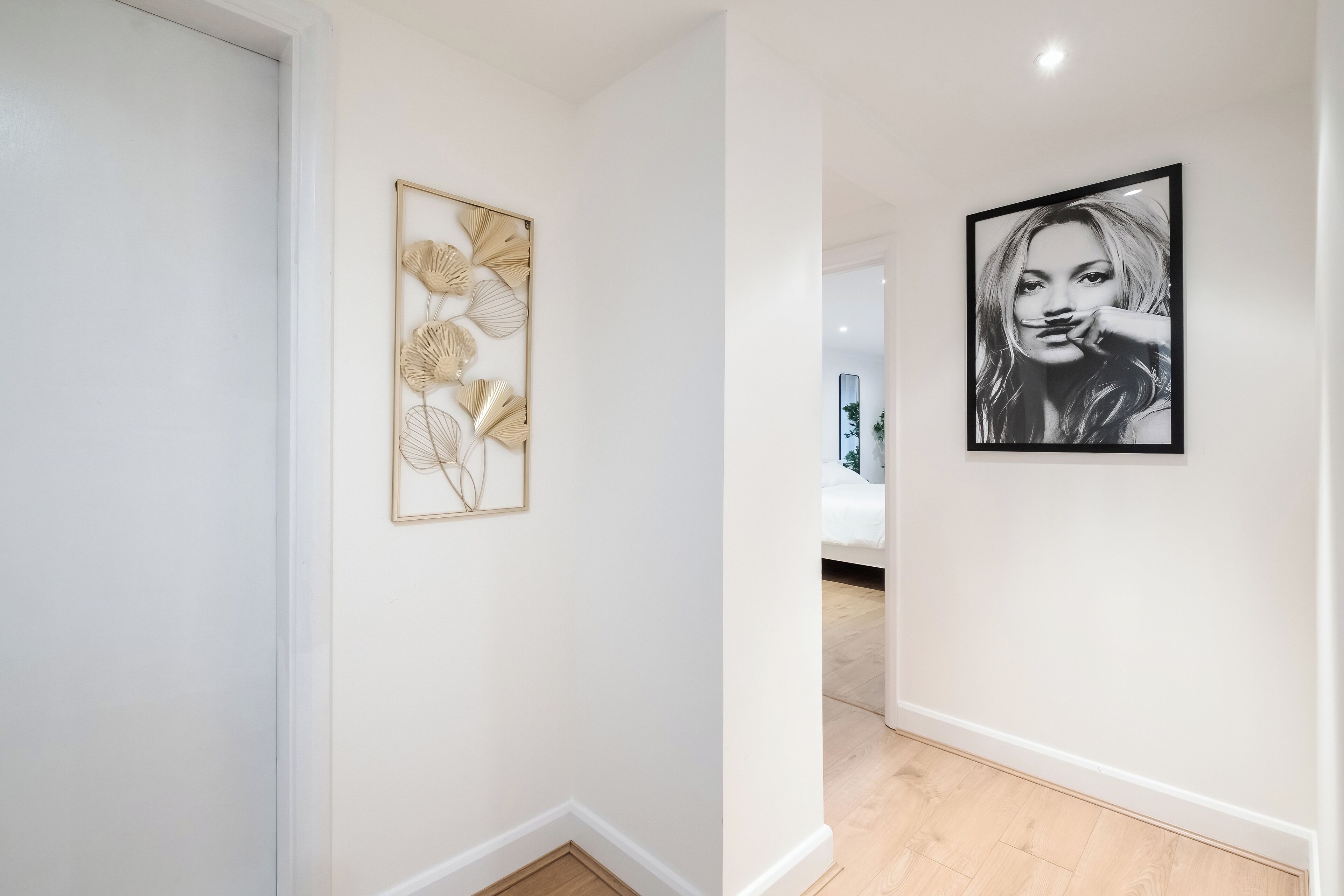 A hallway with a framed artwork of abstract leaves and a black-and-white portrait on the wall.