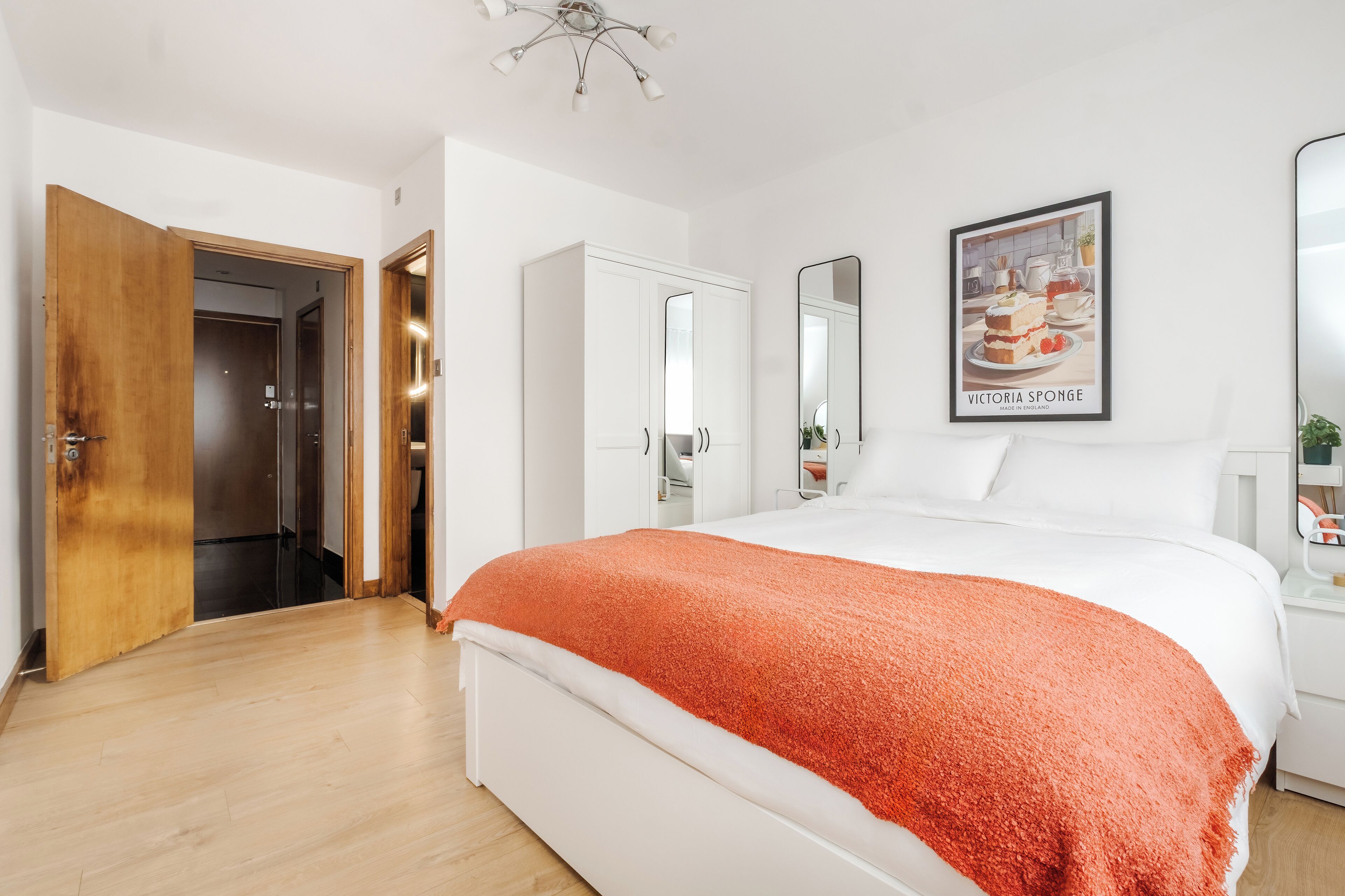A bedroom with a bed, a wooden door, a white wardrobe, and a framed picture on the wall.