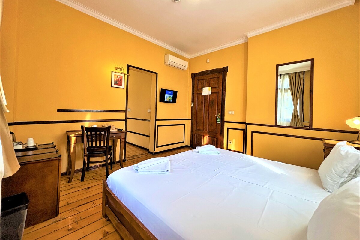 A hotel room with a wooden bed, a desk with a chair, a television, and a window with curtains.