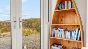 Ein Zimmer mit einem großen Fenster, einer Holzbücherregal und einem Steinfußboden.