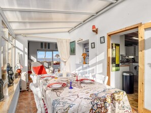 En matplats med ett bord dukat för två personer, utsikt över havet genom fönstret och ett kök som syns genom en öppen dörr.