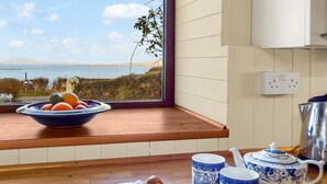 Eine Küche mit Meerblick, eine Fruchtschale, Croissants und blaue und weiße Keramiktassen sowie ein Teekessel.
