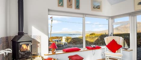 A cozy room with a wood-burning stove, large windows, a comfortable chair, and a view of the outdoors.