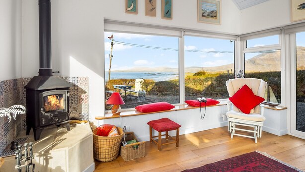 Ein gemütlicher Raum mit Kaminofen, einer Bank mit roten Kissen und Blick auf das Meer.