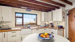 Eine Küche mit weißen Schränken, einer Holzbalkendecke und einem großen Fenster mit Blick auf einen Strand.
