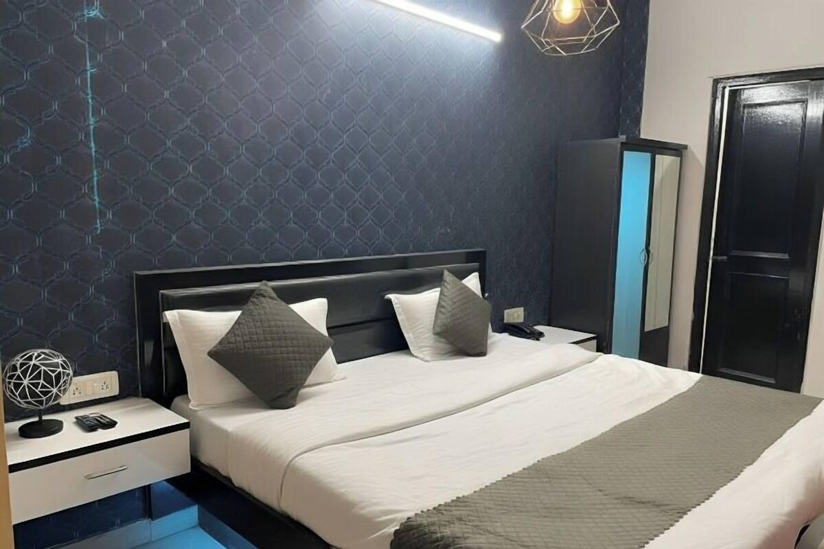 A modern bedroom with a dark patterned wall, a bed with white and gray bedding, a nightstand with a phone and a decorative sphere, and a wardrobe with a mirror.