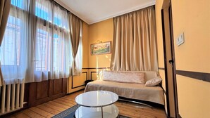 Hotelkamer met een bed, een klein rond tafeltje, een raam met gordijnen, een schilderij aan de muur en een houten vloer.